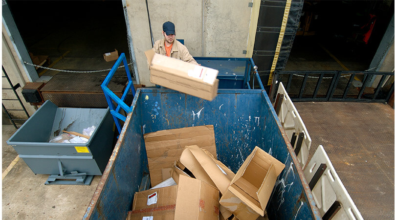 Mann vor Abfallcontainer bei der Entsorgung seiner Verpackungsmaterialien und Abfälle