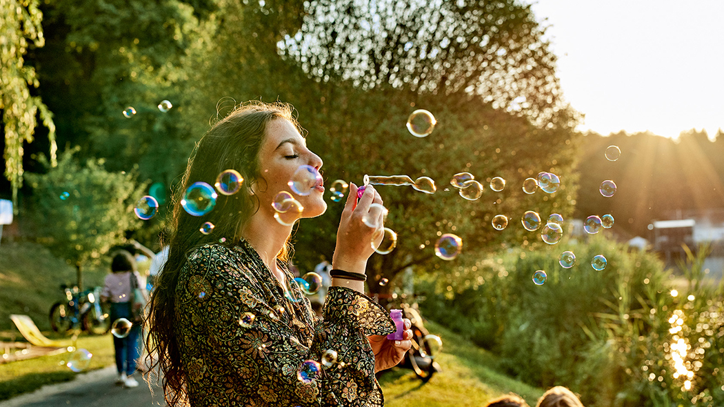 Eine junge Frau macht Seifenblasen in einem Park im Sommer.