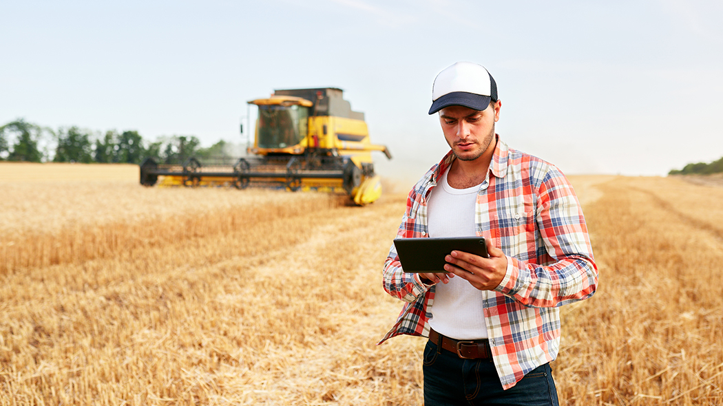 A farmer with a tablet controls a drone across a field