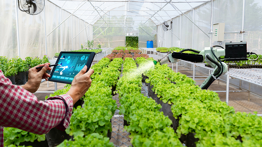 Tablet user in a greenhouse controls a connected irrigation system.