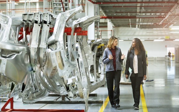 Zwei Frauen in einer Produktionsanlage stehen neben Bauteilen eines Fahrzeugs
