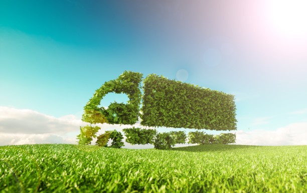 A truck digitally modeled from green leaves drives across a green field, blue sky can be seen in the background.