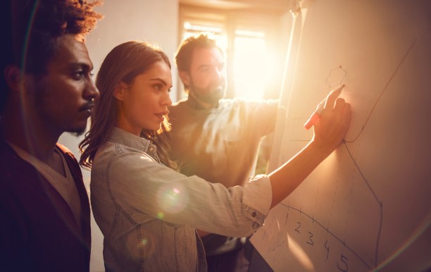 Personen arbeiten zusammen an einem Whiteboard.