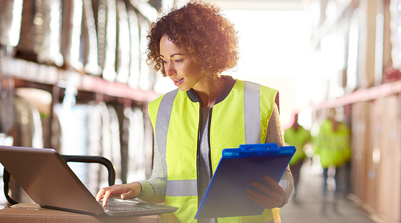 Woman working with laptop and clipboard in warehouse