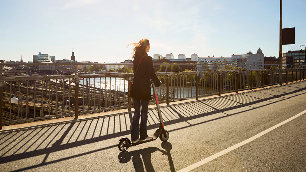 Frau fährt mit E-Scooter über eine Brücke