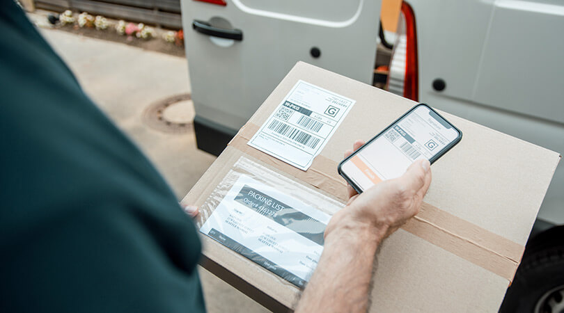 Person holds digital delivery slip on smartphone and package with delivery slip in hands