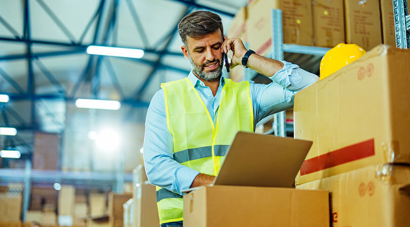 Man with phone and laptop in warehouse managing inventory