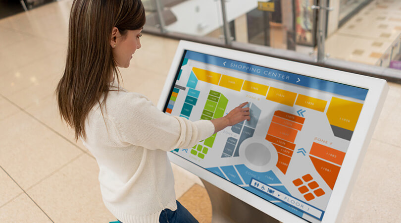 Eine Frau bedient eine digitale Werbetafel in einem Einkaufszentrum.