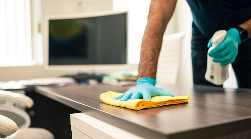 Cleaner wipes desk in office with cleaning cloth.