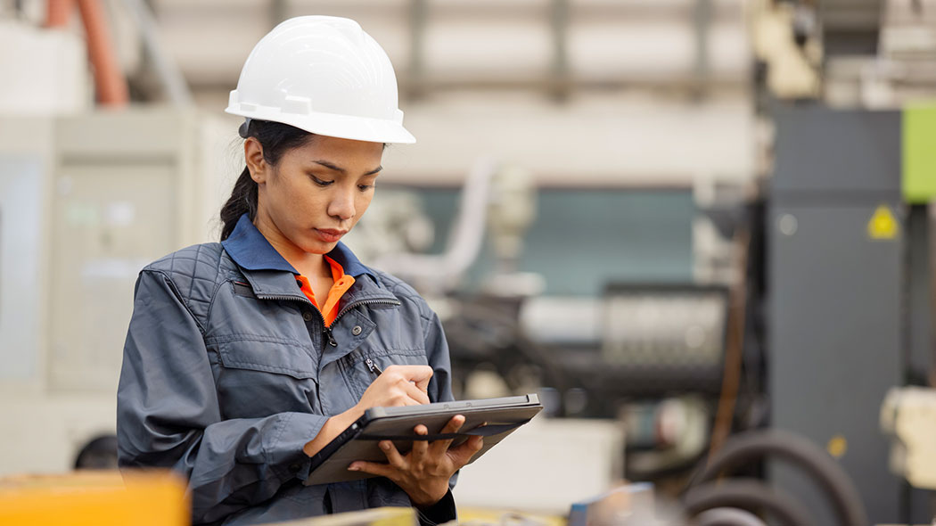 Woman with helmet in factory hall makes notes on a tablet