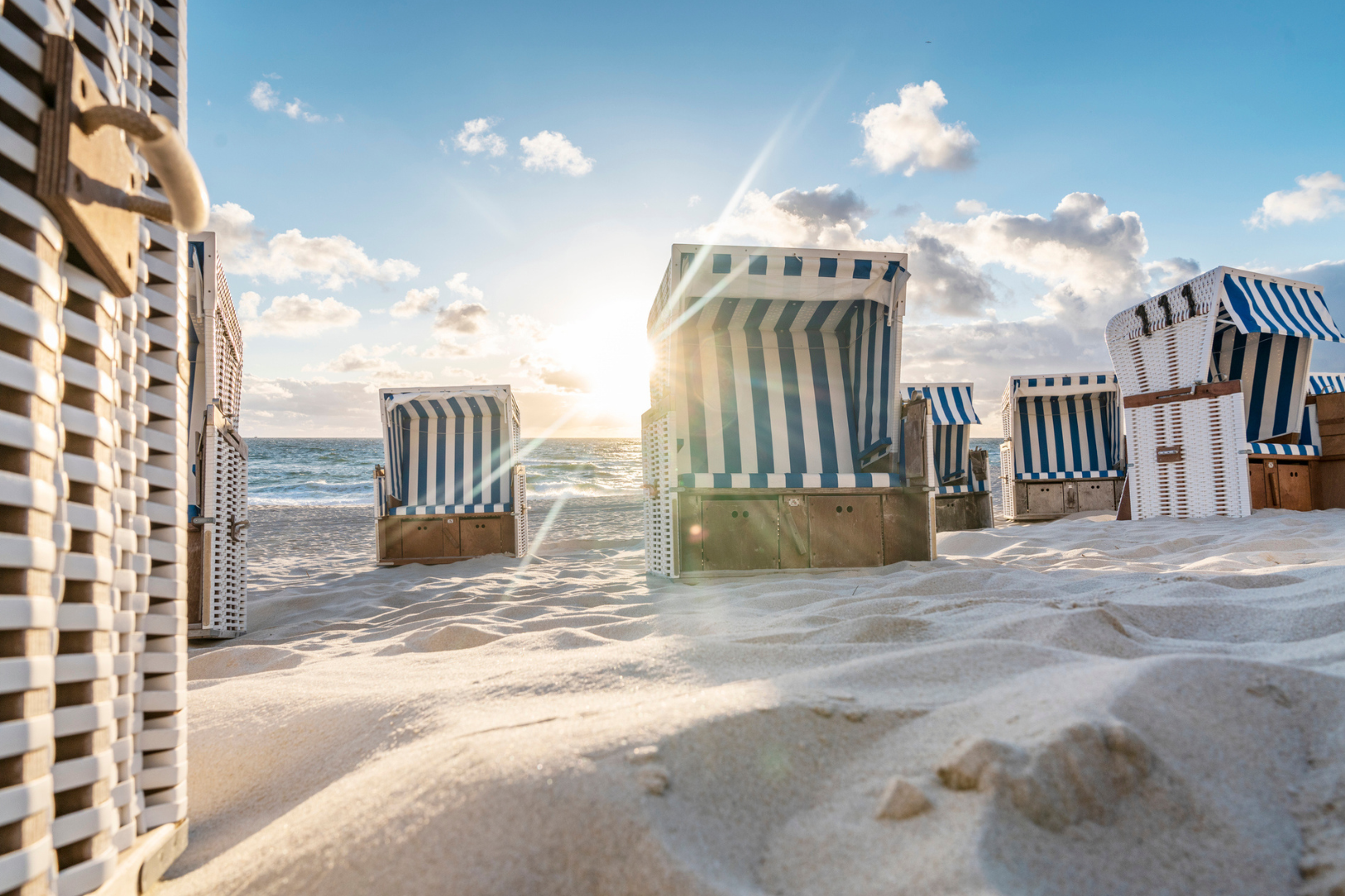 Beach chairs on sand with sea and blue sky in the background.