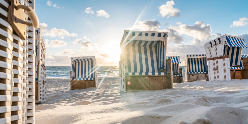 Strandkörbe auf Sand mit Meer und blauem Himmel im Hintergrund.