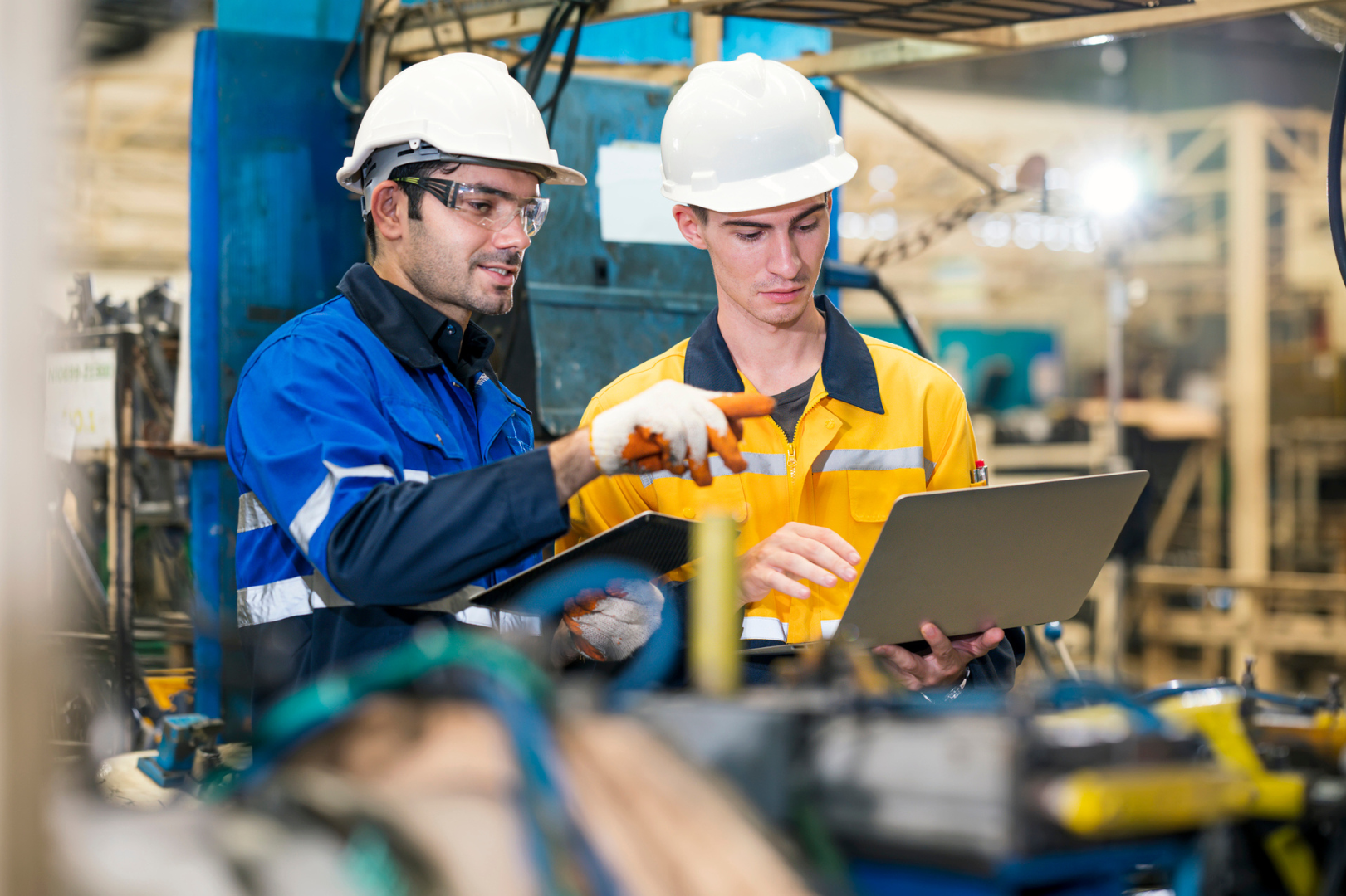 Zwei Arbeiter mit Schutzhelmen prüfen Daten auf einem Laptop in einer Fabrik