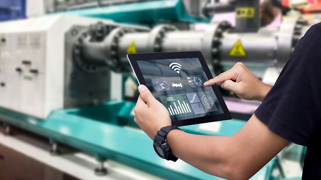 Hände halten Tablet auf Automationsmaschine im Hintergrund.