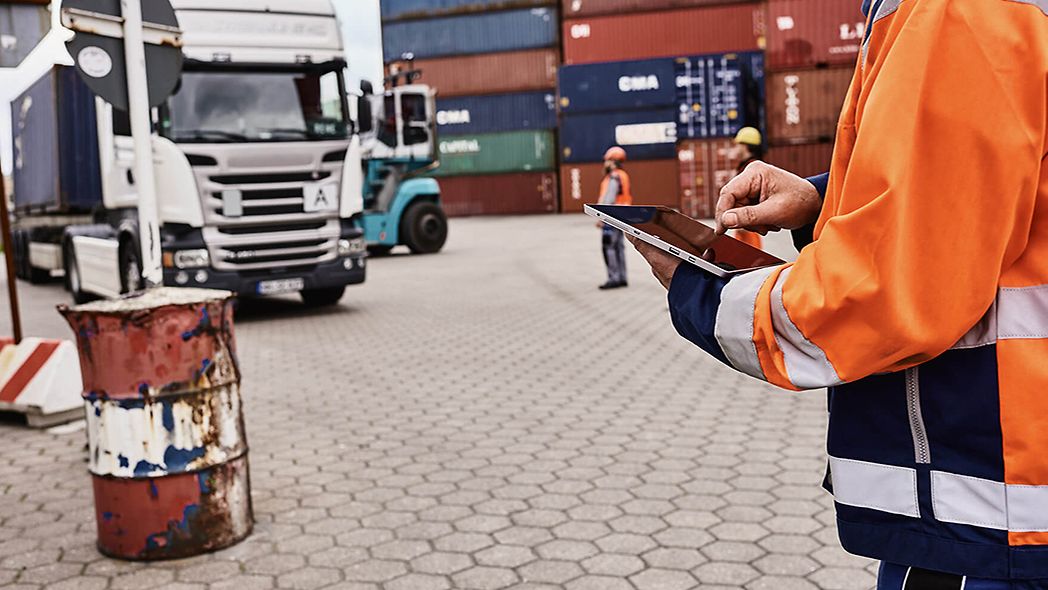 Mann mit Warnschutzjacke koordiniert LKW und Container im Hafen