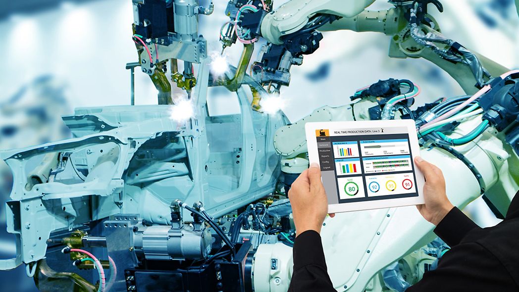 Man with tablet stands in front of an industrial robot of the automotive industry