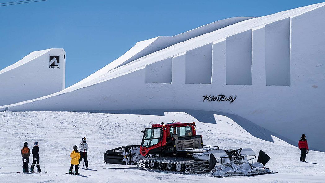 PistenBully von Kässbohrer mit Snowboardfahrern vor Kulisse der Nines