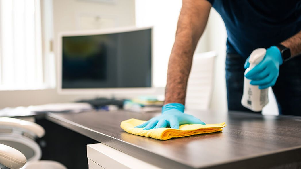 Reinigungskraft wischt Schreibtisch im Büro mit Putzlappen.