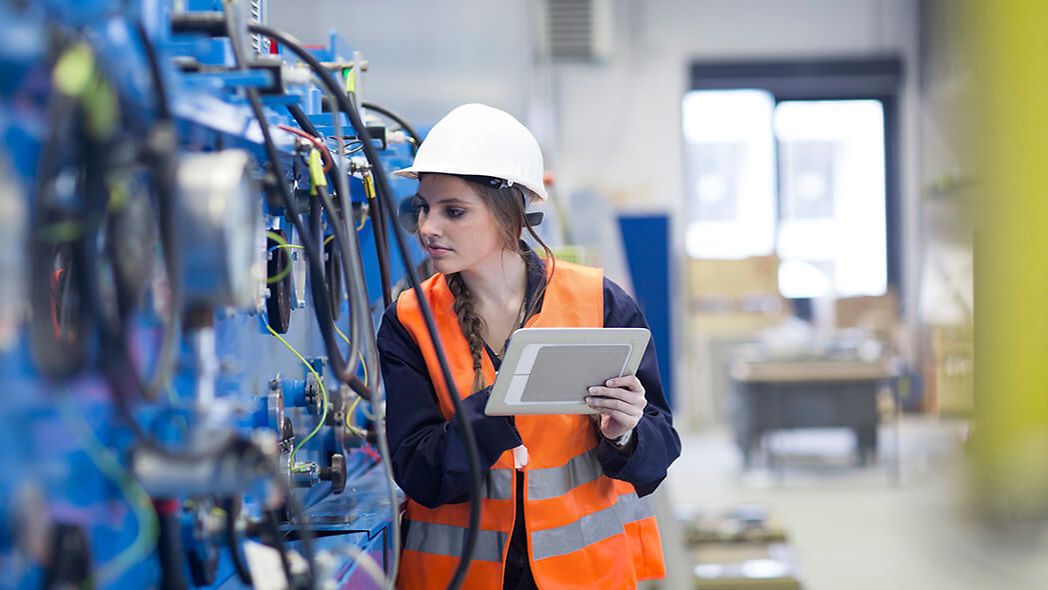 Technikerin mit Tablet überprüft Maschine in Fabrikhalle