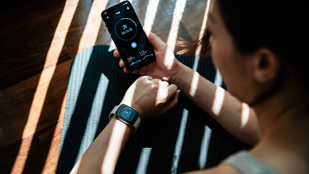 Young athlete looks at smartwatch and her smartphone to check her health data.