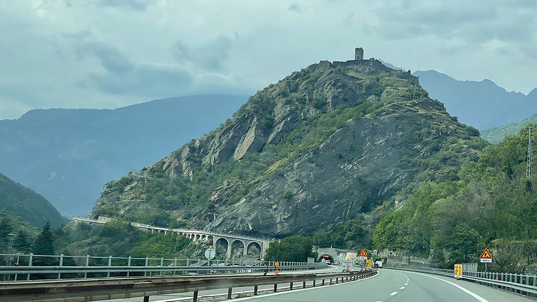 Die Autobahn Richtung Mont Blanc führt in einen Tunnel unter einem Berg mit Burgruine