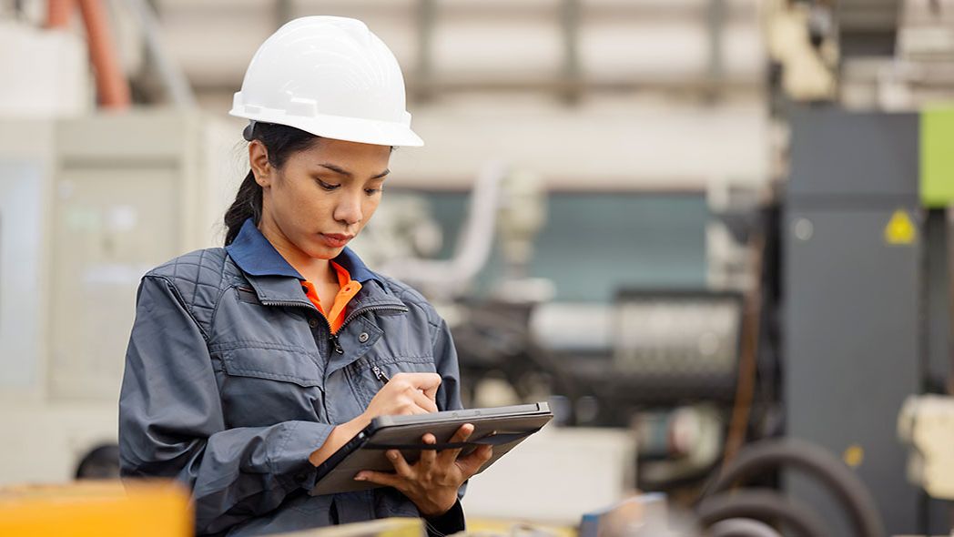 Frau mit Helm in Fabrikhalle schreibt auf ein Tablet