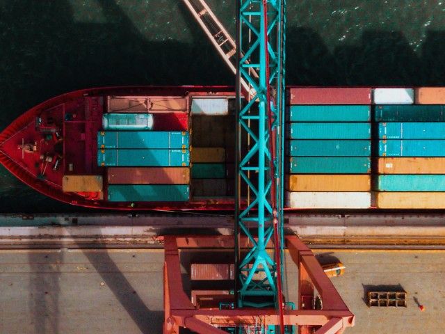 Containerschiff mit bunten Containern und Kran aus Vogelperspektive.