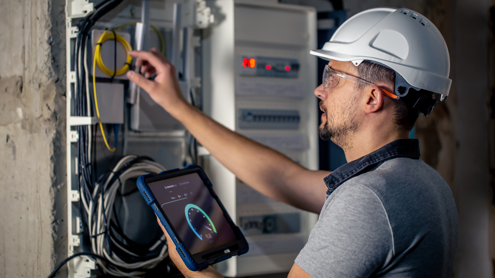 Electrician standing in front of a power cabinet, holding a tablet.