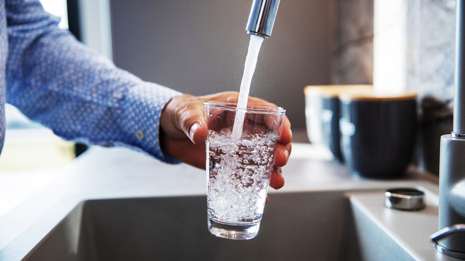 Mensch füllt Glas mit Wasser aus Wasserhahn