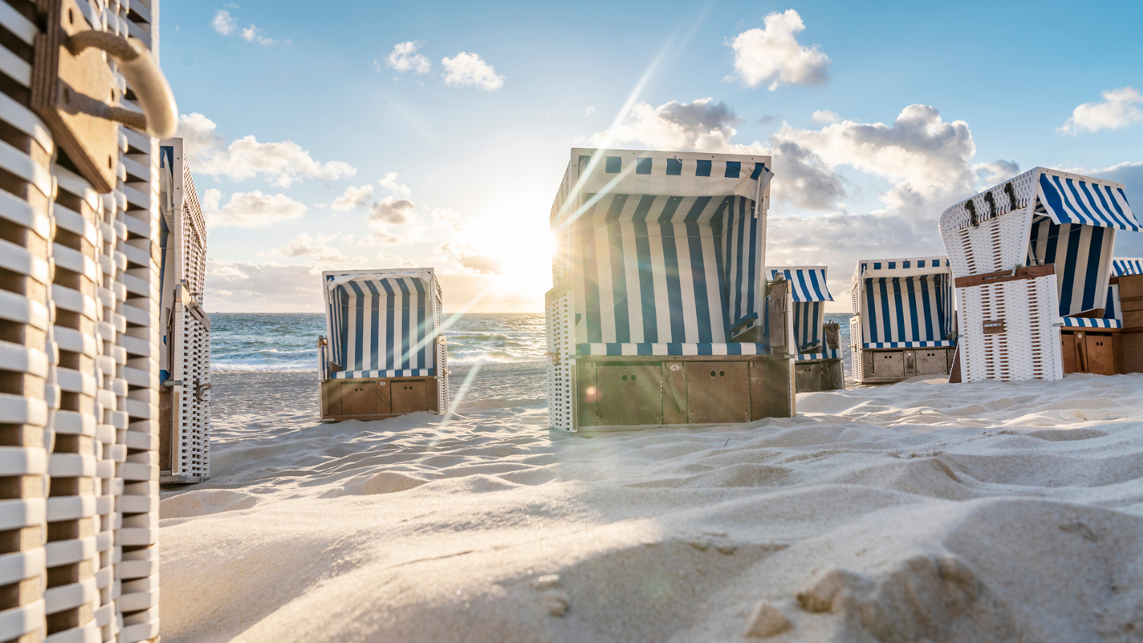 Beach chairs on sand with sea and blue sky in the background.