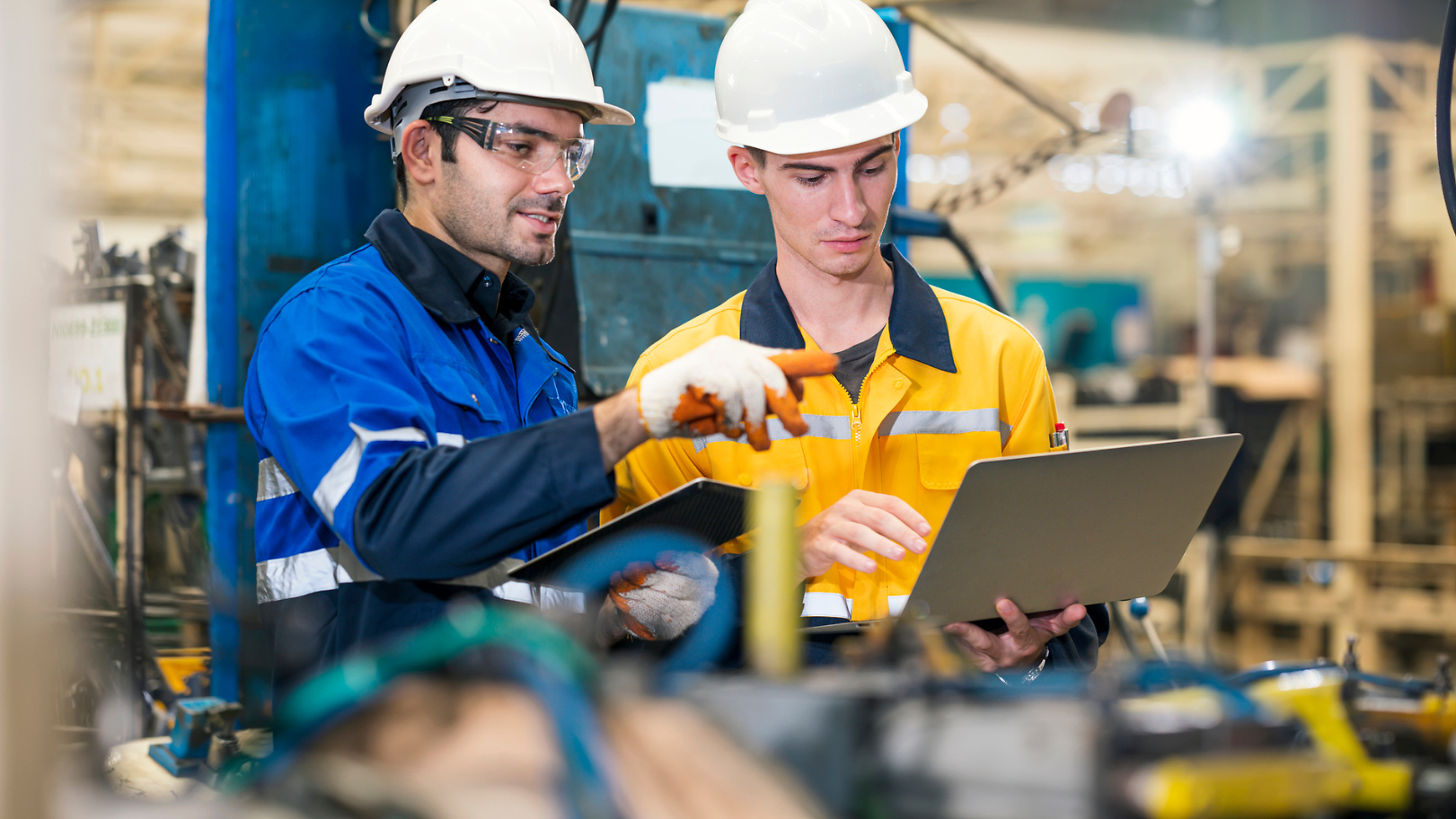 Two workers in hard hats reviewing data on a laptop in a factory