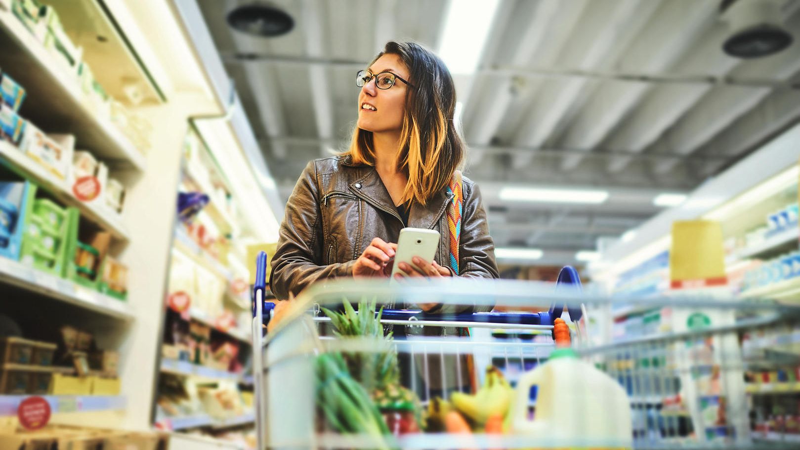 Frau mit Einkaufswagen blickt auf ein Regal im Supermarkt.