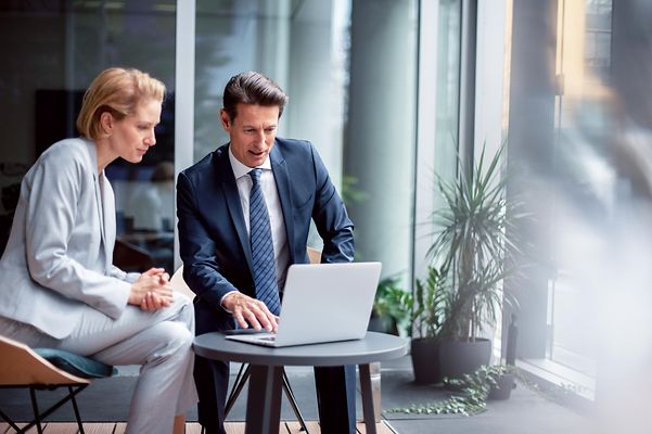 Two business professionals in a modern office environment are reviewing Telekom’s IoT reference cases on a laptop.