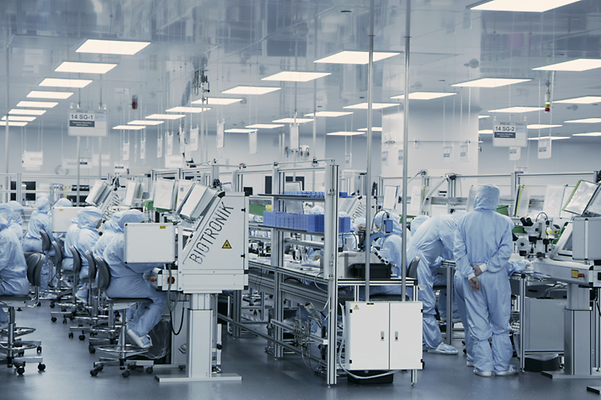 Workers in blue protective suits operate machinery in a modern, clean factory.