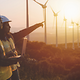 Two people wearing protective helmets in front of wind turbines.