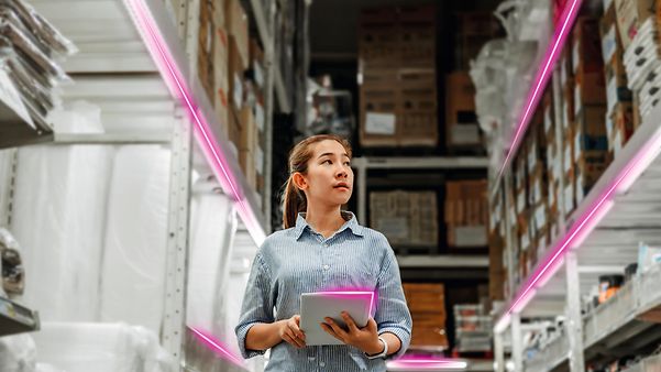 A woman uses the low-cost tracker in a warehouse with high shelves and magenta-lit aisles.