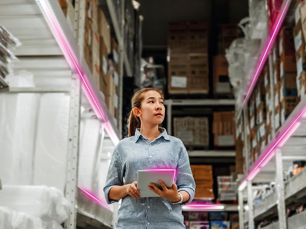 A woman uses the low-cost tracker in a warehouse with high shelves and magenta-lit aisles.