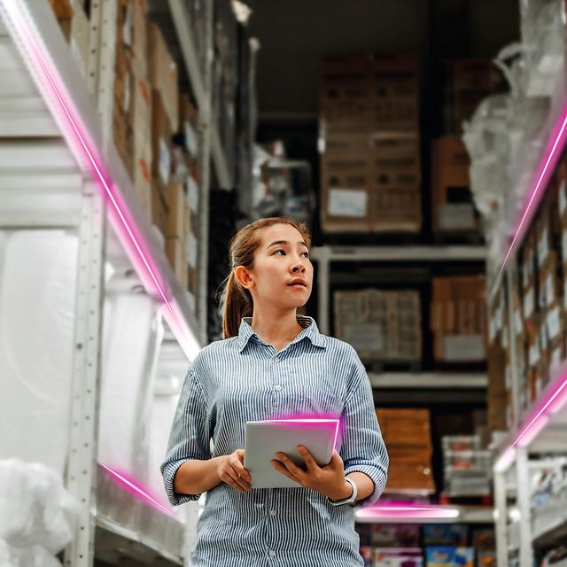 A woman uses the low-cost tracker in a warehouse with high shelves and magenta-lit aisles.