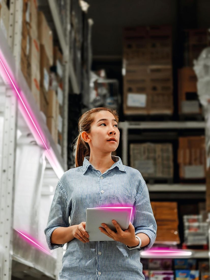 A woman uses the low-cost tracker in a warehouse with high shelves and magenta-lit aisles.