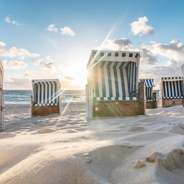 Strandkörbe auf Sand mit Meer und blauem Himmel im Hintergrund.
