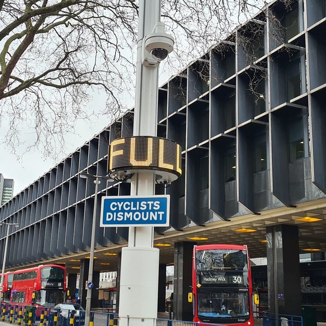 Grafik von einer Straße mit parkenden und fahrenden Autos, Straßenlaternen, einem Pakhaus und abstrakten bunten Linien.