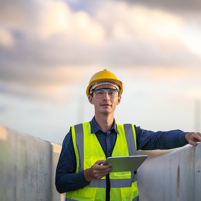 Mann mit Sichereitsweste und Helm hält ein Tablet in der Hand.