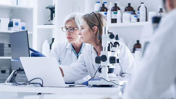 Two female scientists in lab coats look together at a laptop in a laboratory.