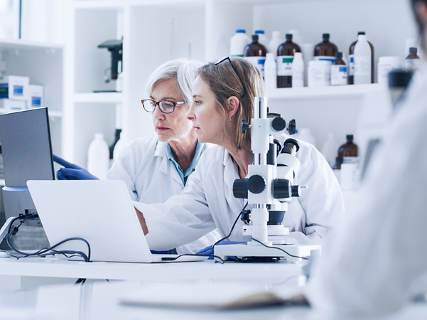 Two female scientists in lab coats look together at a laptop in a laboratory.