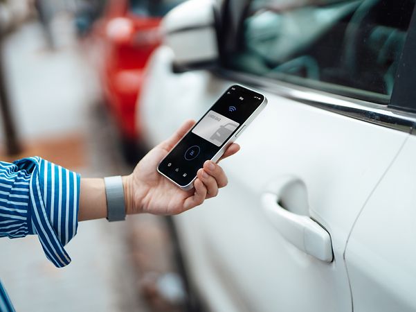 Nahaufnahme einer jungen Frau, die mit einer Handy-App auf ihrem Smartphone ihr Auto entriegelt.