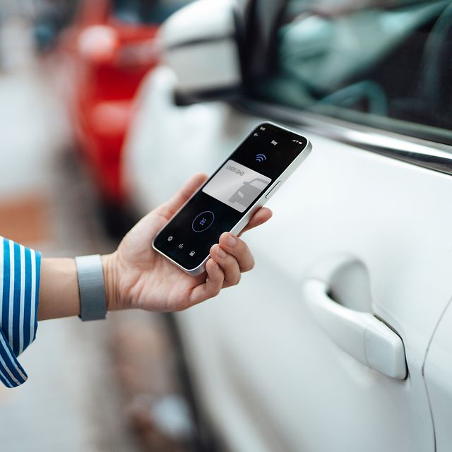 Nahaufnahme einer jungen Frau, die mit einer Handy-App auf ihrem Smartphone ihr Auto entriegelt.