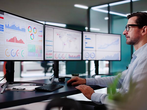 Man at a desk with three monitors showing diagrams and graphs of the M2M Service Portal