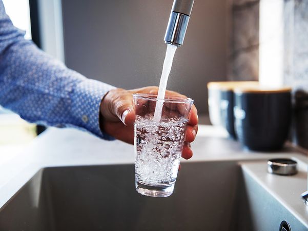Person filling a glass with water from a tap.