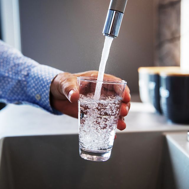 Person filling a glass with water from a tap.
