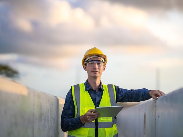 Man with safety waistcoat and helmet holding a tablet.